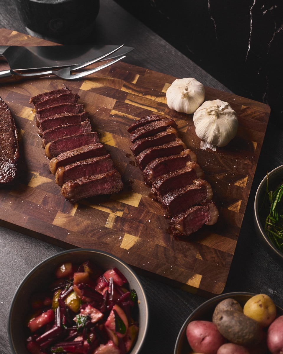 Sliced seared steak on a wooden board with garlic and roasted potatoes